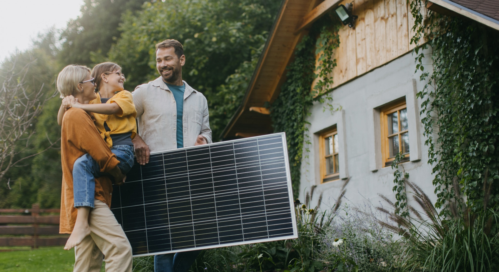 Family walking in garden holding solar panel. Solar energy and sustainable lifestyle of young family